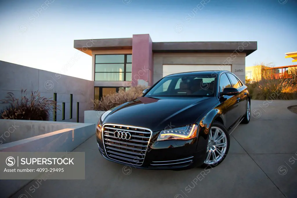 Front 3/4 static view of a black 2012 Audi A8 parked in the driveway of an ultra modern home at dusk.