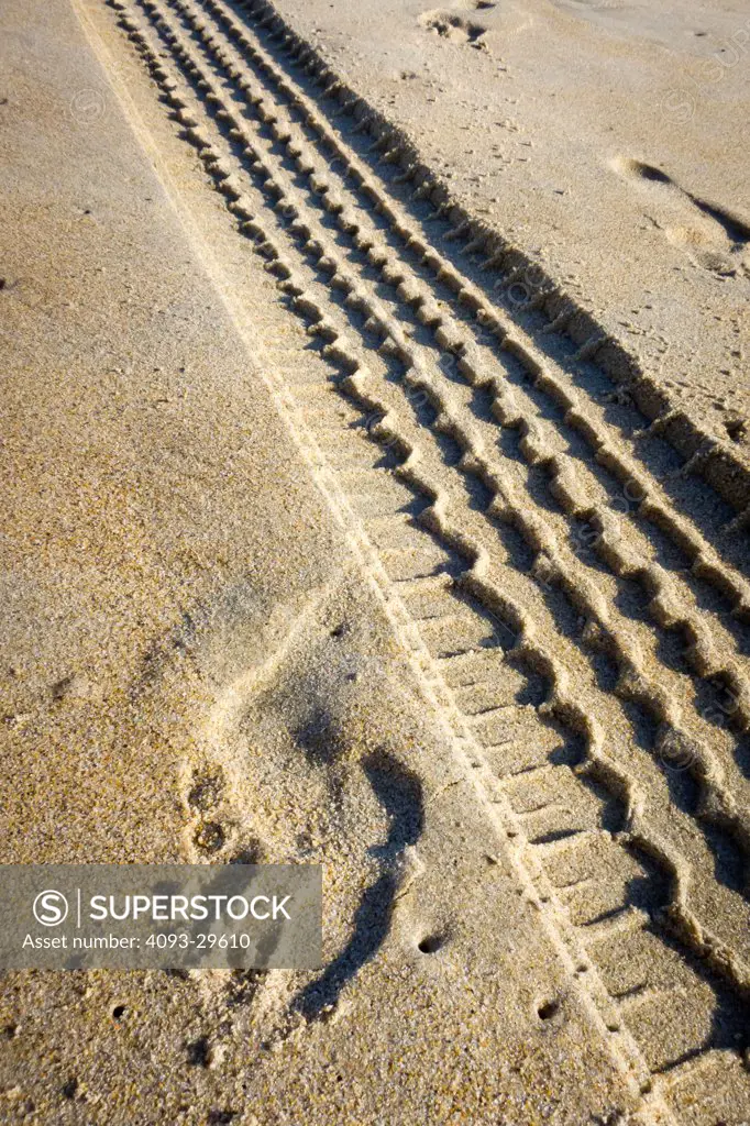 Tire tracks on a sandy beach in the afternoon with children walking away.