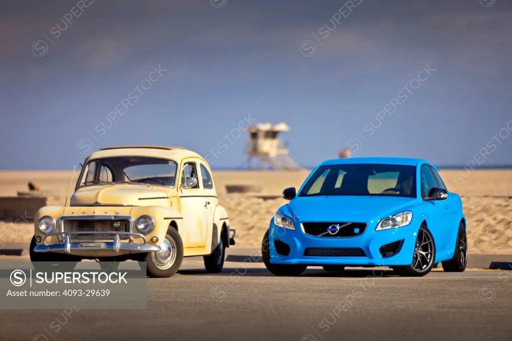 Front 3/4 static view of a blue 2013 Volvo C30 T5 Polestar parked next to a yellow 1958 Volvo PV544 at the beach.