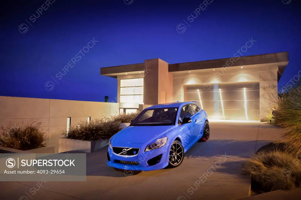 Front 3/4 static of a blue 2013 Volvo C30 T5 Polestar parked in the driveway of a modern house at night or dusk.
