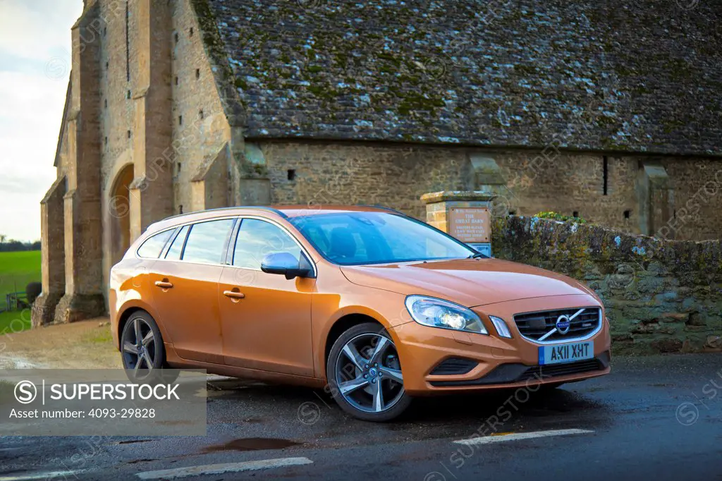Front 3/4 static of an orange 2013 Volvo V60 wagon with DRIVe diesel engine parked next to a rural stone church