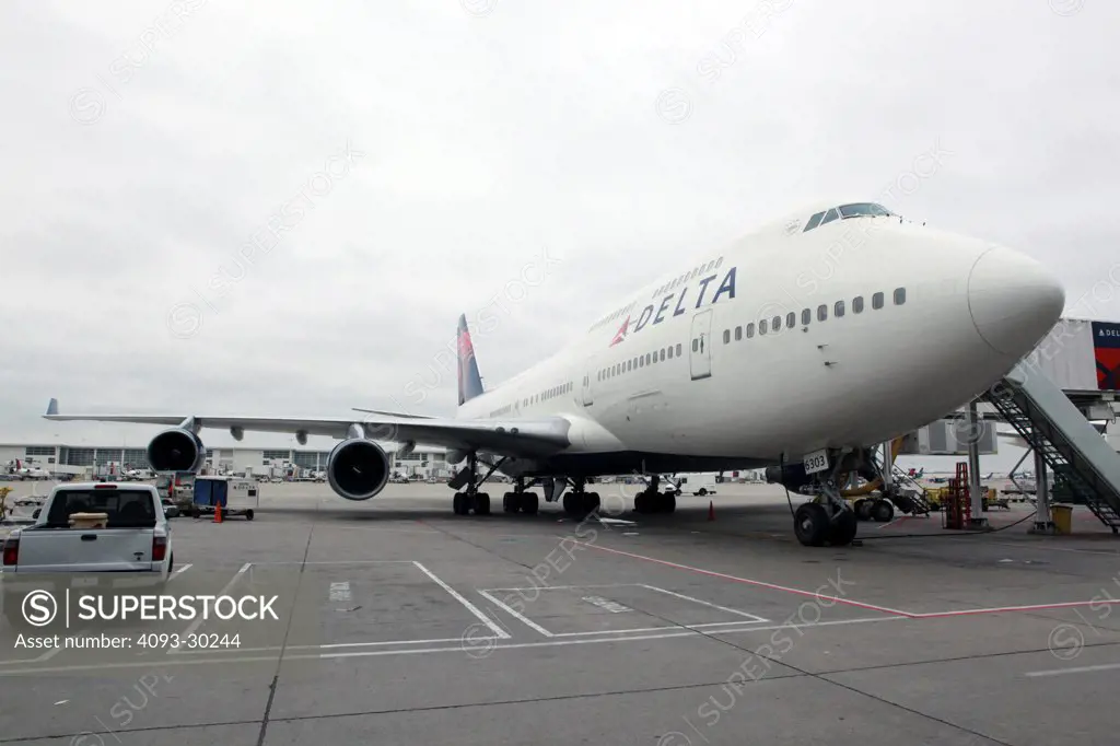 Front 3/4 view of a 2012 Delta Airlines Boeing 747-400 parked on the ramp or tarmac at an airport gate.