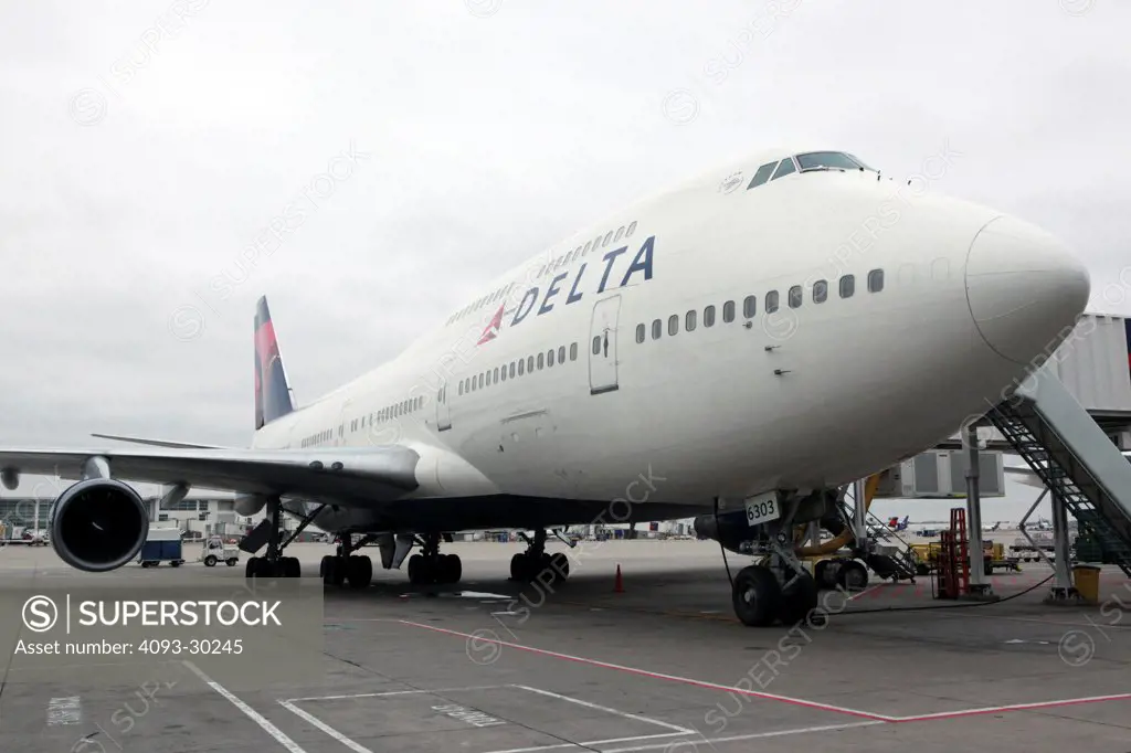 Front 3/4 view of a 2012 Delta Airlines Boeing 747-400 parked on the ramp or tarmac at an airport gate.