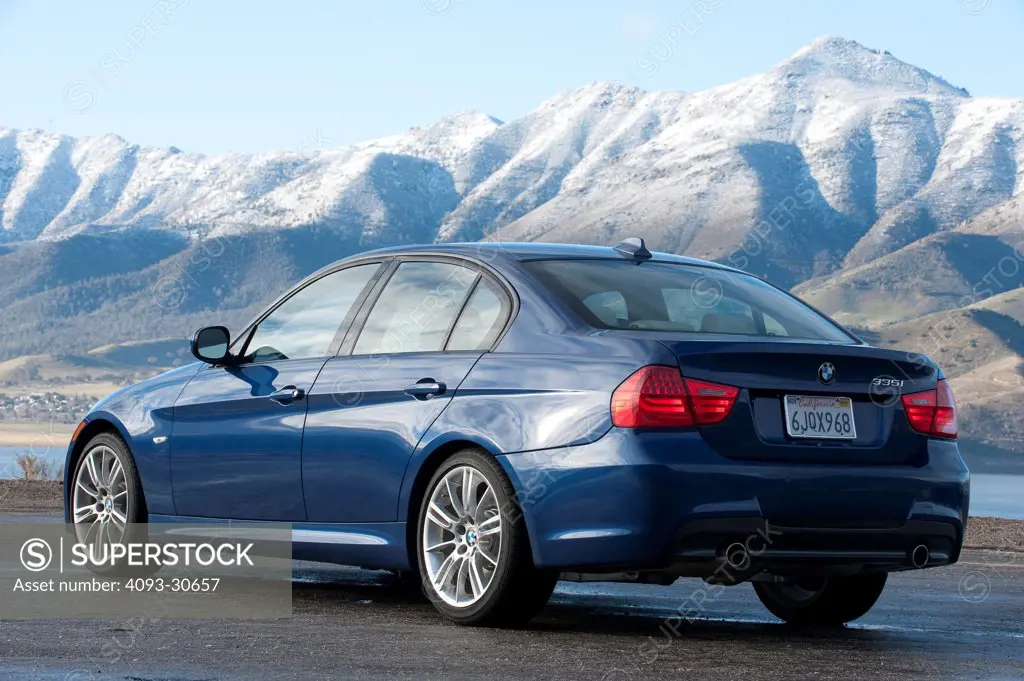 2011 Blue BMW 335i parked on a rural road with mountains in the background, rear 3/4 static view