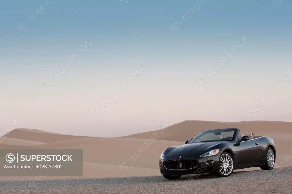 2011 Maserati GranCabrio parked next to sand dunes at dusk, front 3/4 static view
