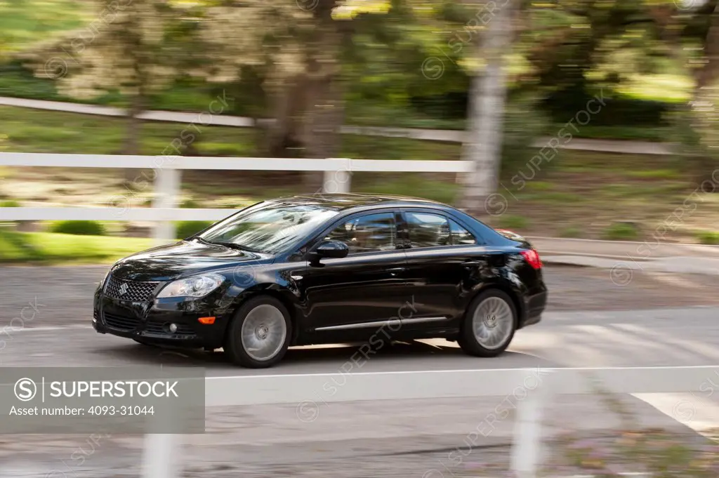 Front 3/4 of a black 2010 Suzuki Kizashi driving along a rural road.