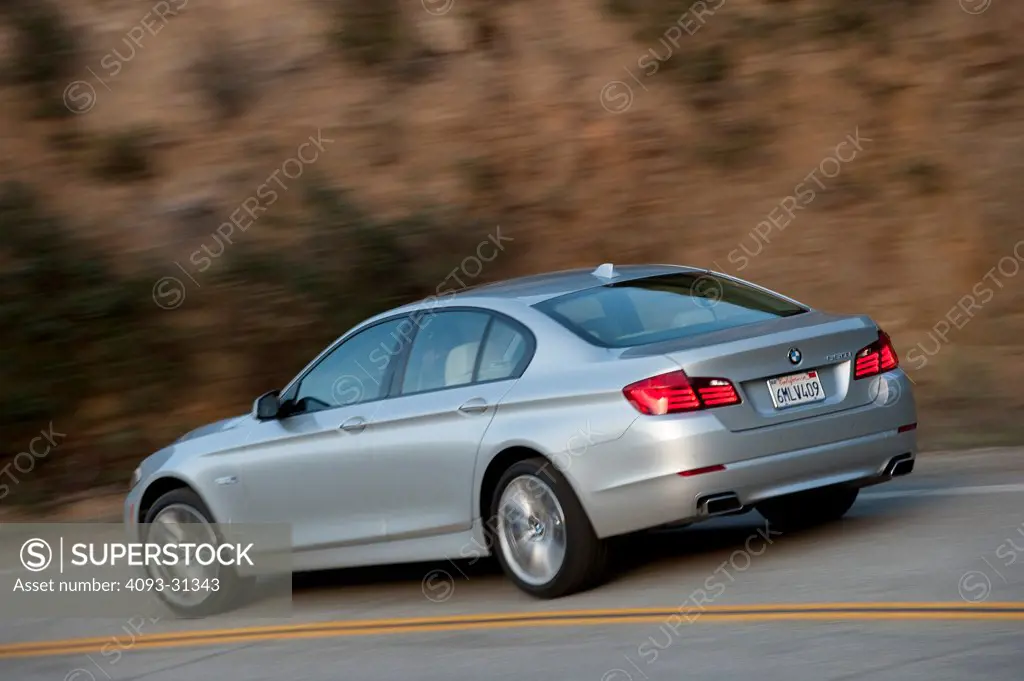 Rear 3/4 of a silver 2012 BMW 550i driving around a curve on a mountain road.