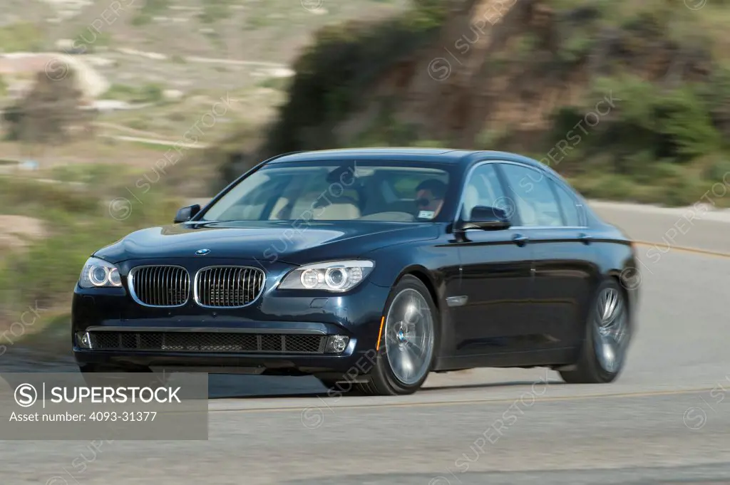 Front 3/4 of a black 2012 BMW 750Li driving around a curve on a mountain road.