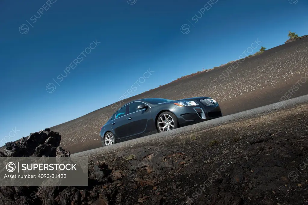 Low angle front 7/8 of a 2012 Buick Regal driving along a deserted road.