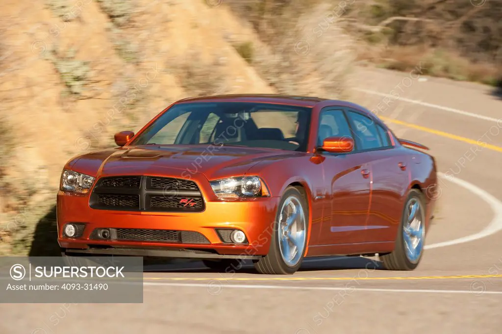 Front 3/4 view of an orange 2012 Dodge Charger R/T driving along a mountain road.