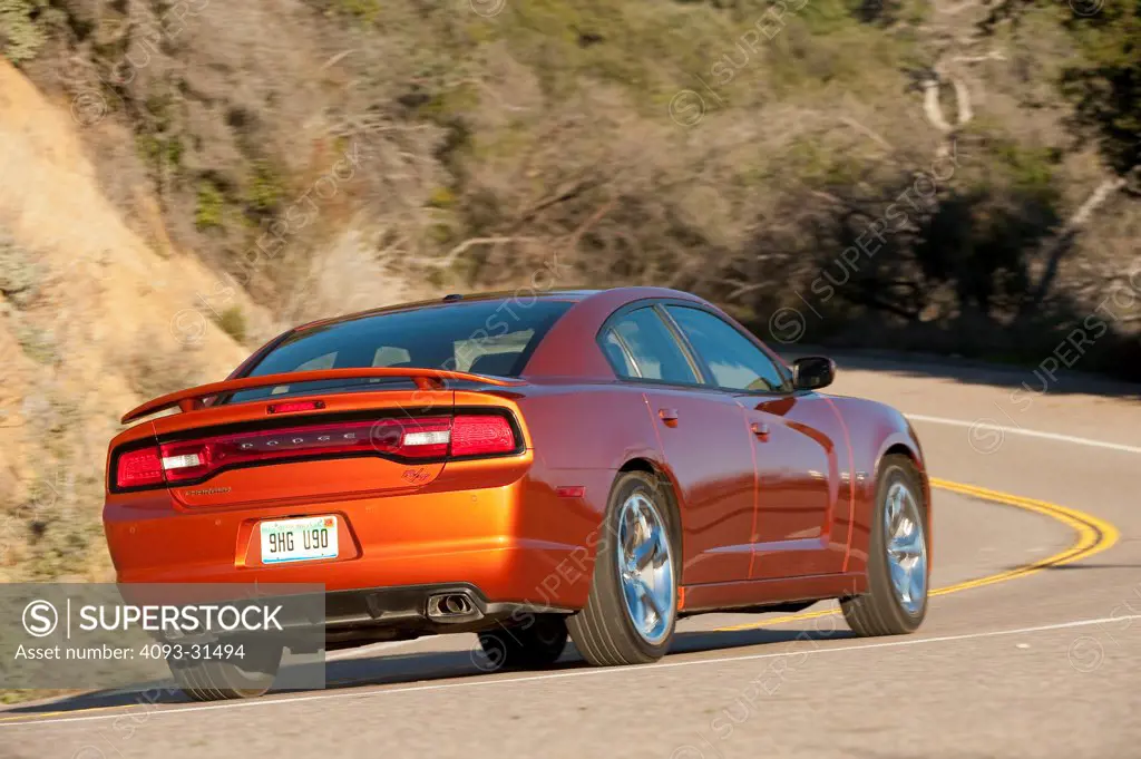 Rear 3/4 view of an orange 2012 Dodge Charger R/T driving along a mountain road.