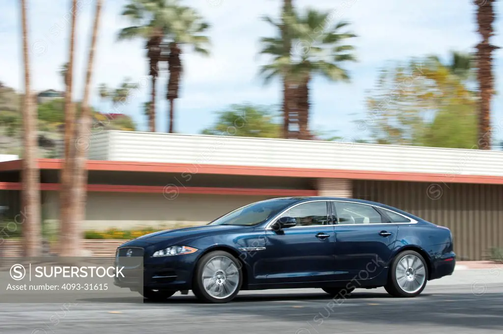 Front 7/8 view of a 2012 Jaguar XJL driving in front of a modern house