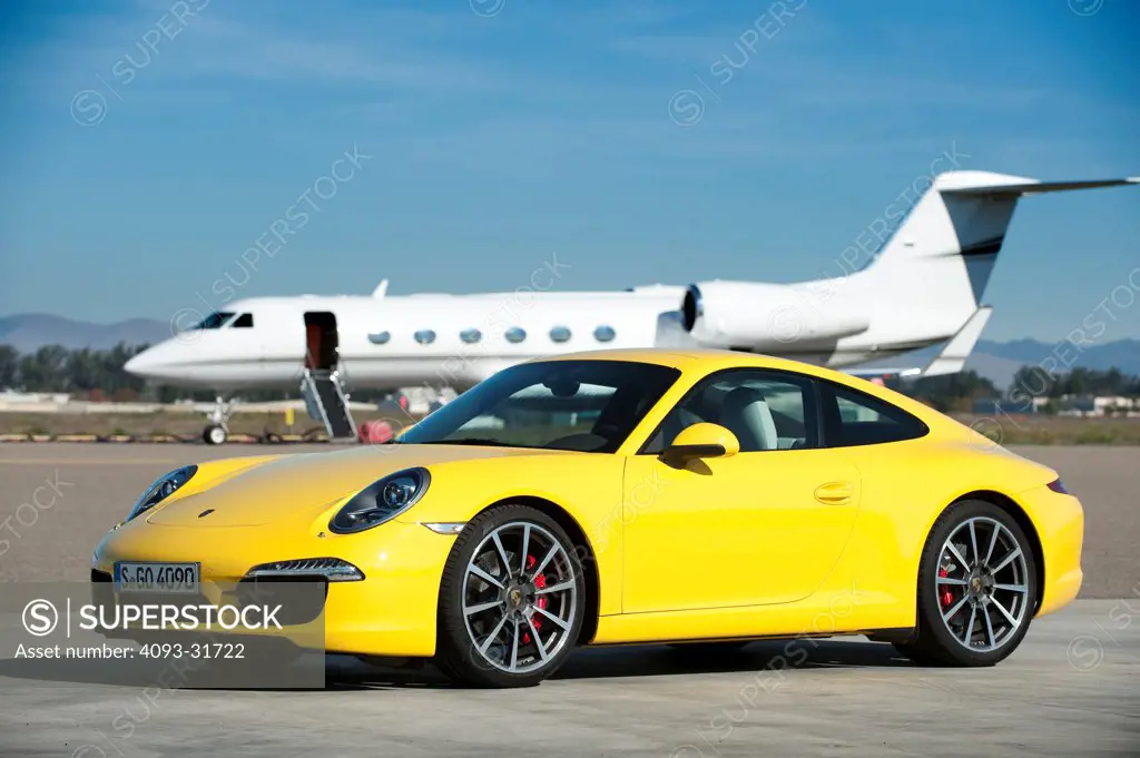 Front 3/4 view of a yellow 2012 Porsche 911 Carrera S. Porsche platform number 991 shown with a jet in the background, parked on a test track.