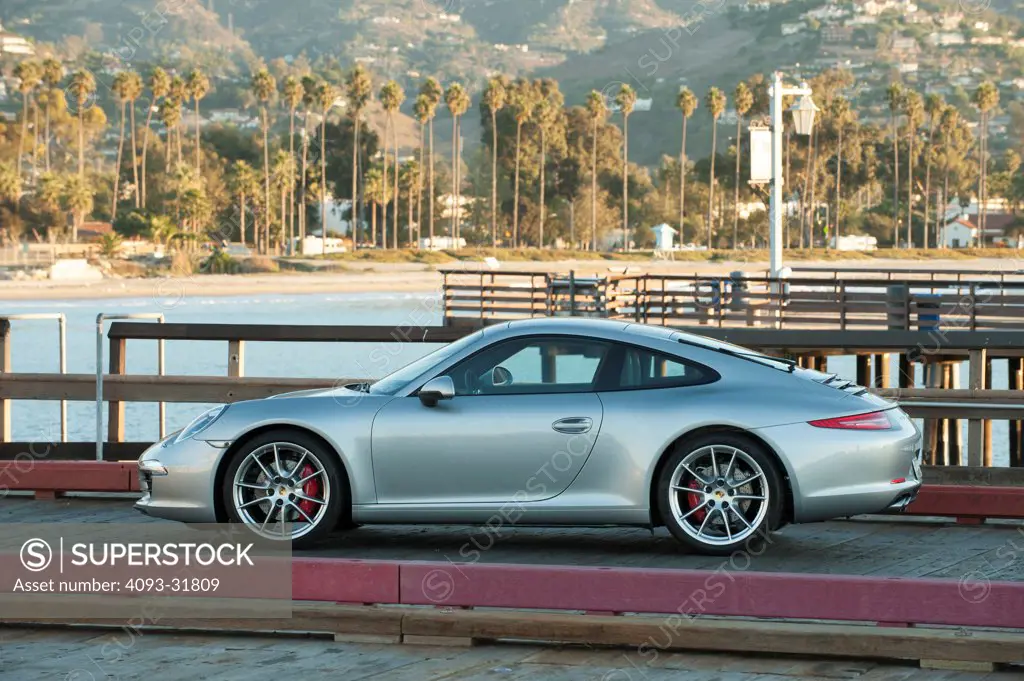 Profile view of a silver 2012 Porsche 911 Carrera S, platform number 991 parked on a pier near the ocean.