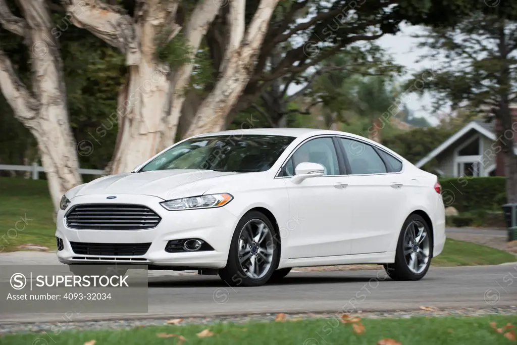 Front 3/4 view of a white 2013 Ford Fusion Titanium driving through a suburban neighborhood.