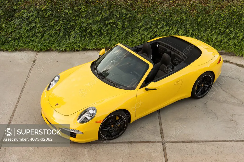 High angle front 3/4 view of a yellow 2013 Porsche 911 Carrera S Cabriolet parked in a driveway.