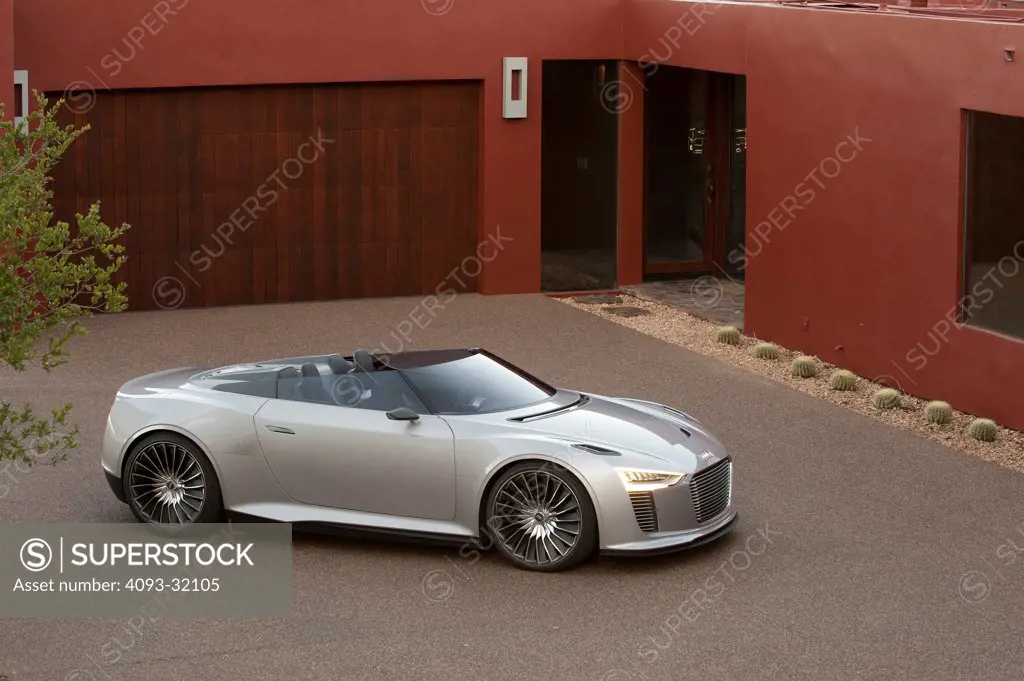 Front 7/8 view of a convertible silver Audi e-tron Spyder Concept parked in front of a red house.