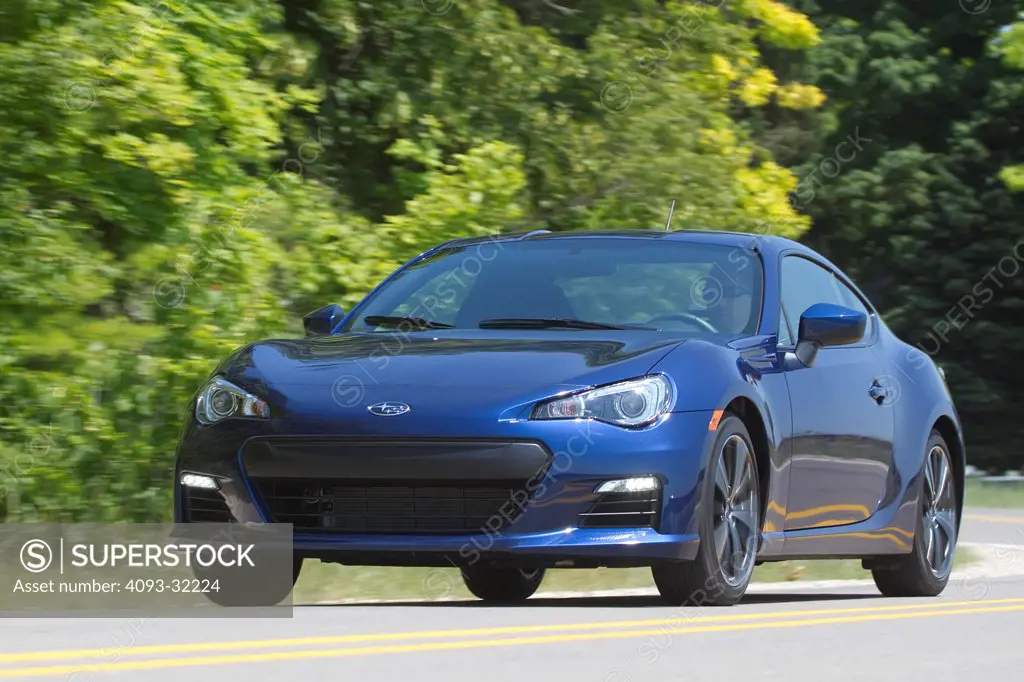 Front 3/4 view of a blue 2013 Subaru BRZ driving along a rural road.
