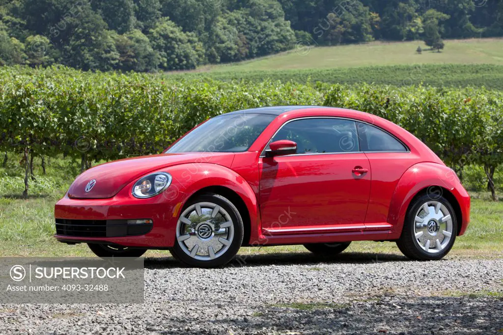 Front 3/4 static view of a red 2012 Volkswagen Beetle parked on a rural, gravel road.