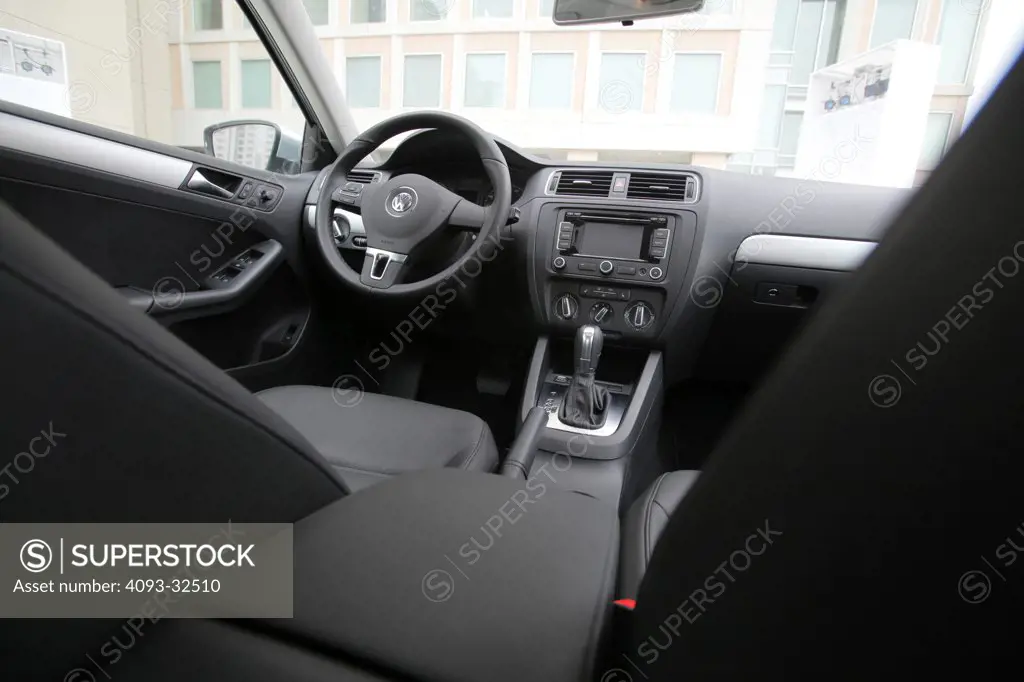 Low angle interior view of a 2012 Volkswagen Jetta GLI showing the instrument panel, steering wheel, dashboard, center console, multi function display, climate controls, gear shift lever and black leather seats.