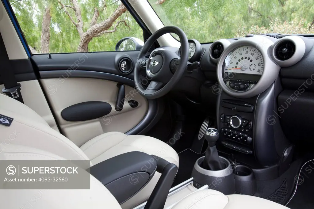 Interior of a 2012 Mini Countryman showing the showing the instrument panel, steering wheel, dashboard, center console, climate controls, gear shift lever and tan leather seats.