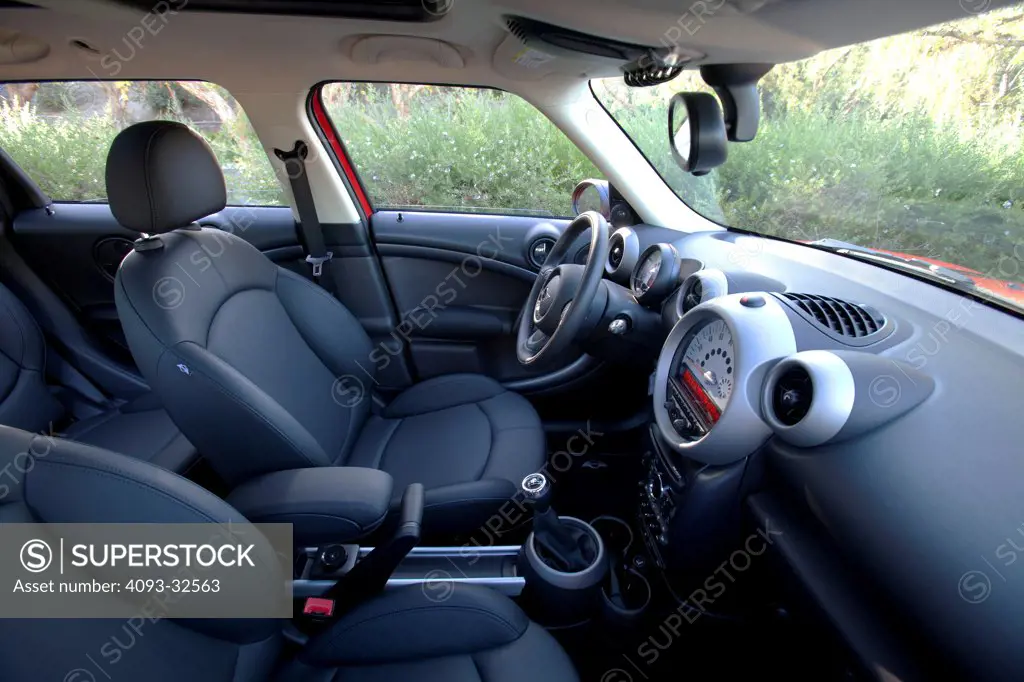 Interior of a 2012 Mini Countryman showing the showing the instrument panel, steering wheel, dashboard, center console, climate controls, gear shift lever and black leather seats.