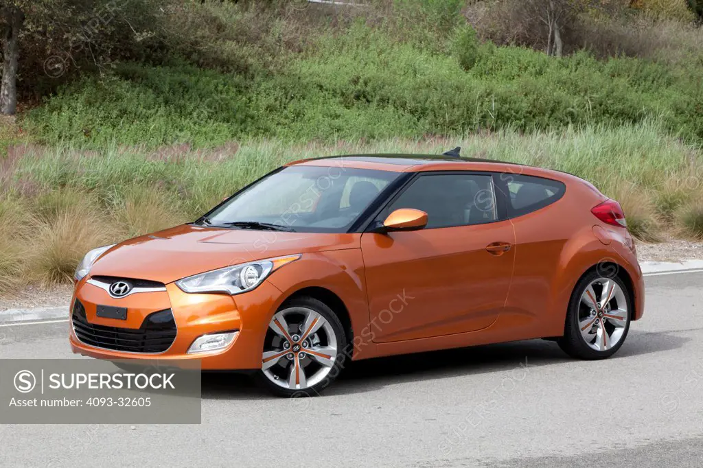 Front 3/4 static of an orange 2012 Hyundai Veloster on a rural road.