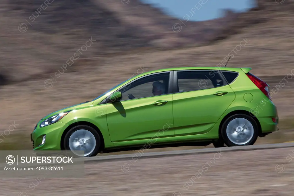 Profile action of a green 2012 Hyundai Accent on a rural mountain road.