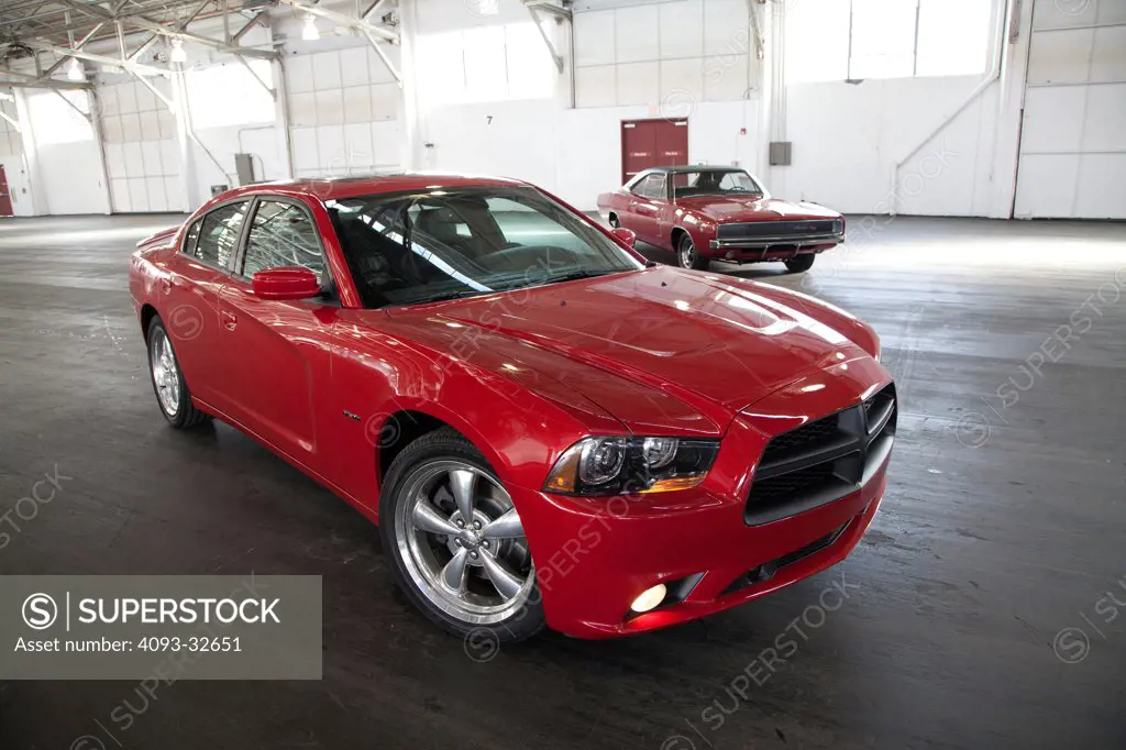 Front 3/4 static view of a red 2012 Dodge Charger R/T HEMI parked inside a warehouse. Classic 1969 Dodge Charger in background.