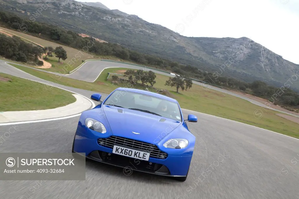 Straight on nose action of a blue 2012 Aston Martin Vantage S on a race track in Europe.