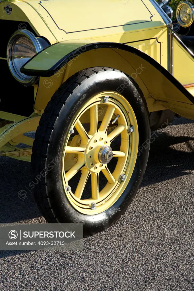 Exterior detail of a classic yellow 1914 Stutz Bearcat antique showing the wooden front left wheel and tire.