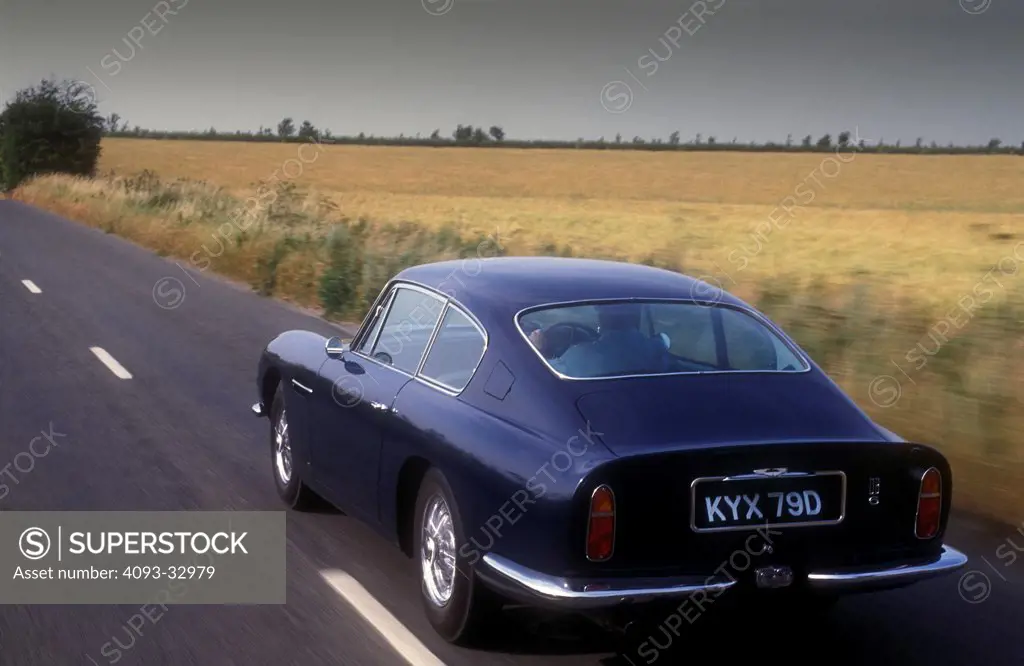 1966 Aston Martin DB6 driving along country road, rear 3/4