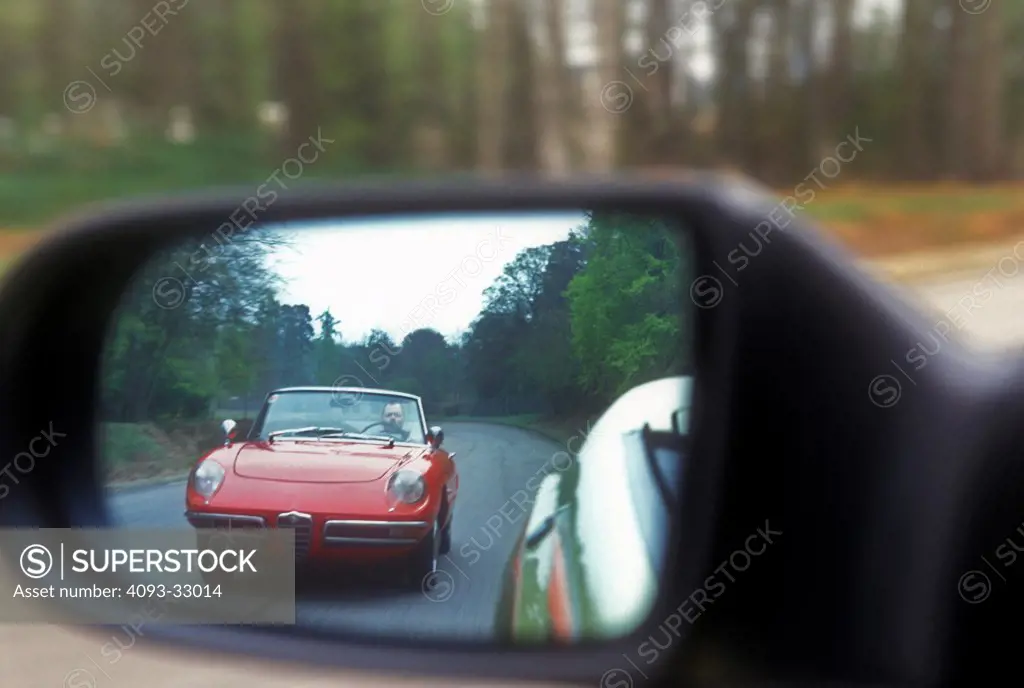 1967 Alfa Romeo Spyder reflected side view mirror on country road, front view