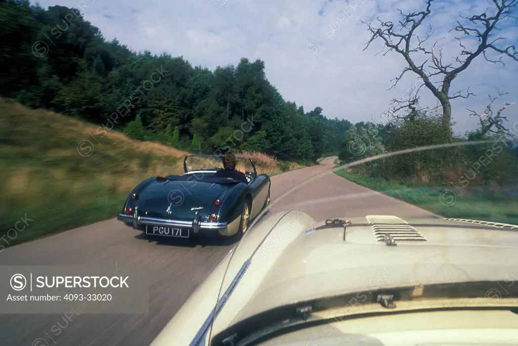 1961 Austin Healey 3000 driving on country road, viewed from behind, rear 7/8