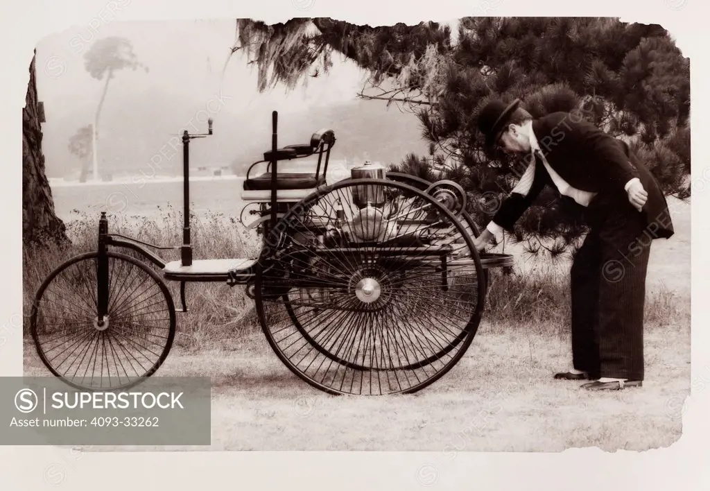 Man turning the flywheel to start a 1886 Benz Motorwagen automobile. This is a modern day reproduction of the first gasoline powered vehicle.
