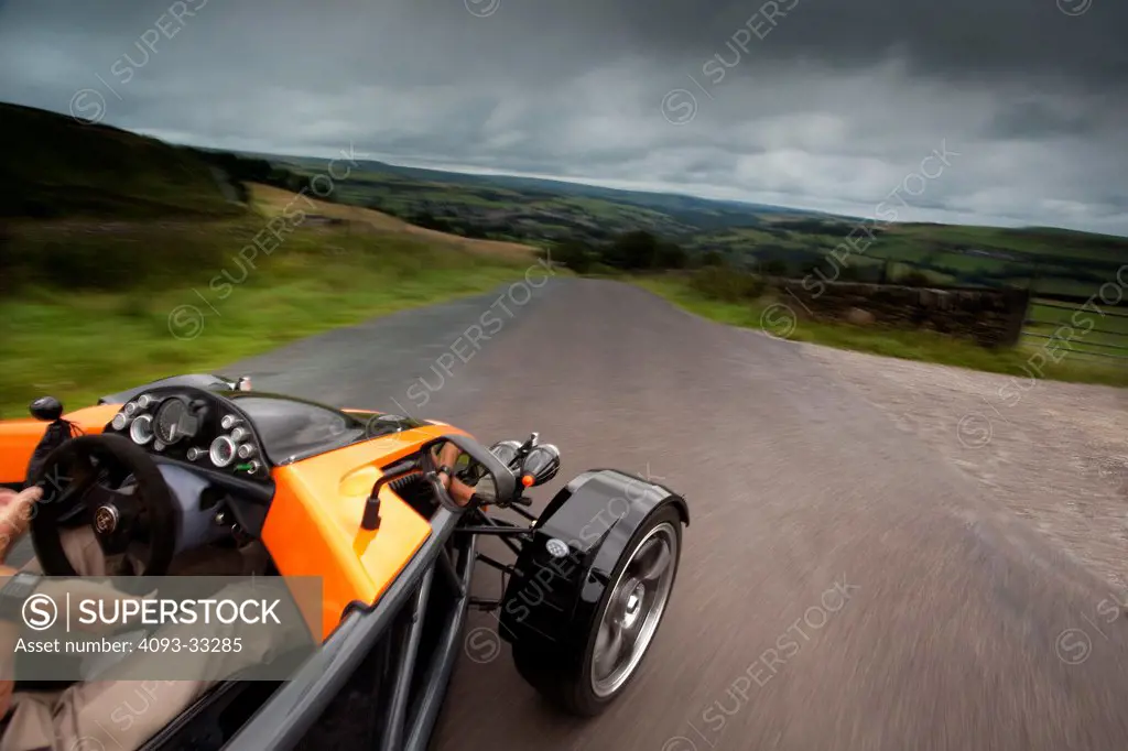 Overhead POV action of an orange 2010 SDR Exoskeleton sports car on a rural road in England UK.