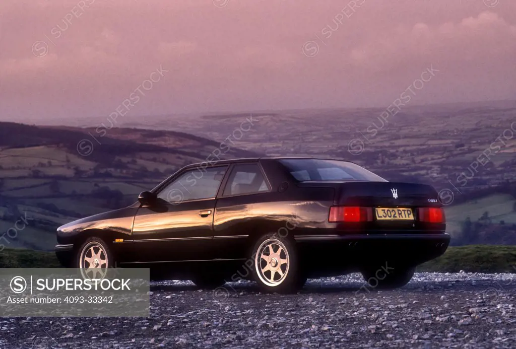 Rear 3/4 static of a black 1994 Maserati Ghibli parked on a gravel road in the Black mountains of Wales, United Kingdom