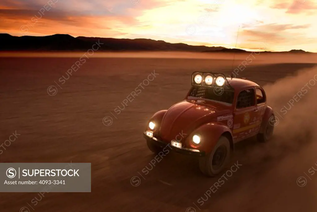 custom off road bug races during sunset with headlights on.