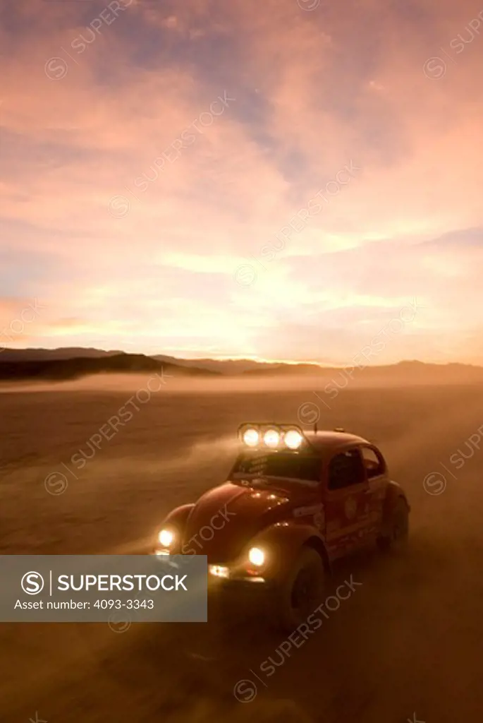 custom off road bug races during sunset with headlights on.
