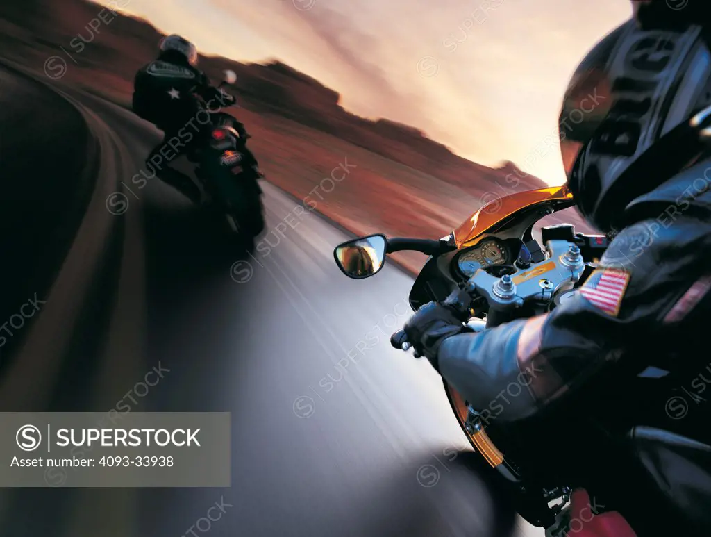 high speed action of two 2010 Buell 1125R motorcycles with riders wearing helmets and leather jackets in a rural desert location at dusk.