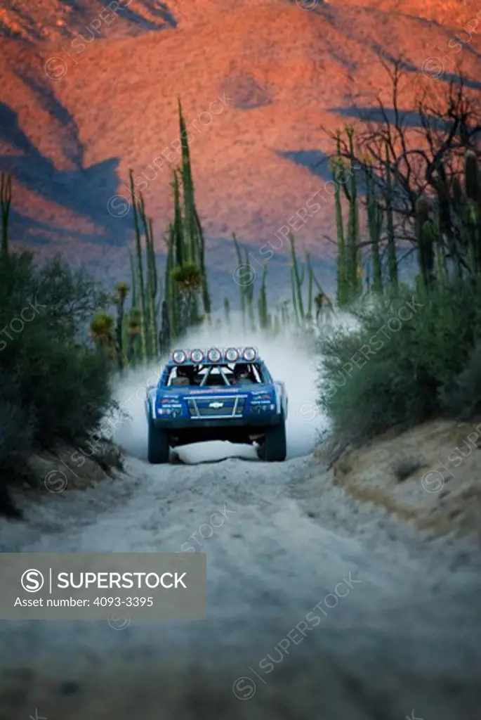 Baja Desert racing truck driving towards the viewer on a dirt road with mountains in the background