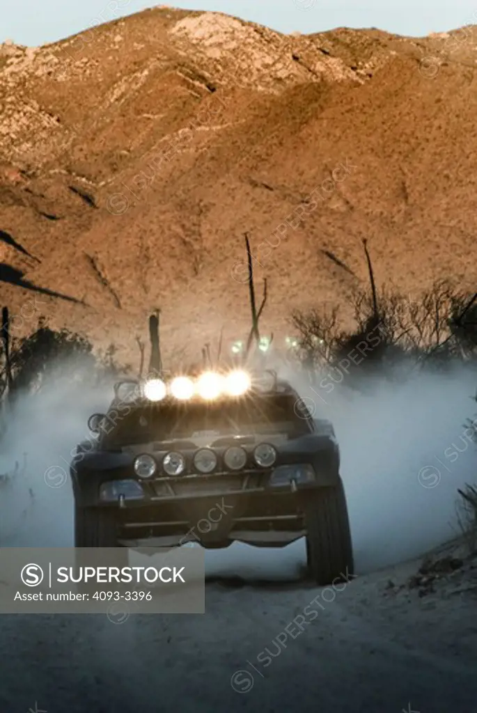Baja Desert racing truck driving towards the viewer on a dirt road with mountains in the background