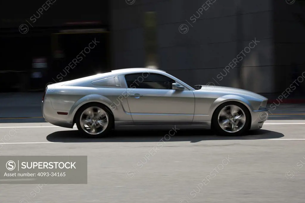 Panning profile action of a silver 2011 Ford Mustang GT Lacotta driving on an urban city street.