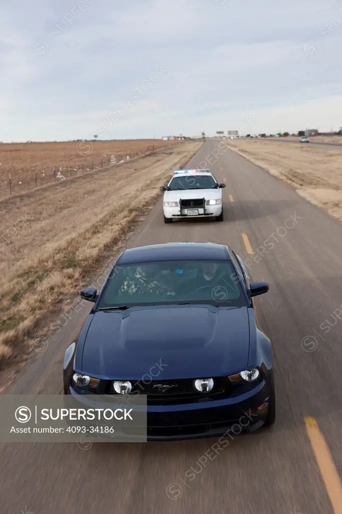 Straight on nose action of a blue 2011 Ford Mustang GT being chased by a 2011 Ford Crown Victoria Police Interceptor on a rural road.