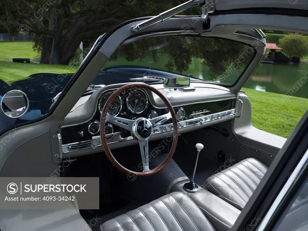 Interior view of a 1954 Mercedes-Benz 300SL Coupe showing the wood steering wheel, instrument panel, dashboard, gear shift lever and gray leather seats.
