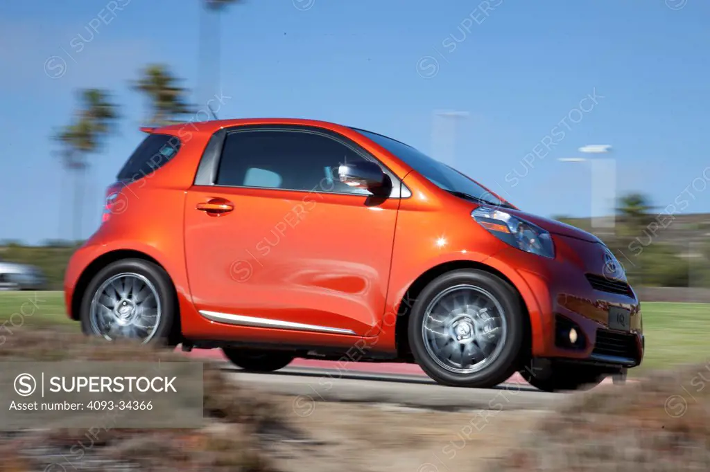 Low, front 3/4 action of an orange 2012 Scion IQ on a rural street.