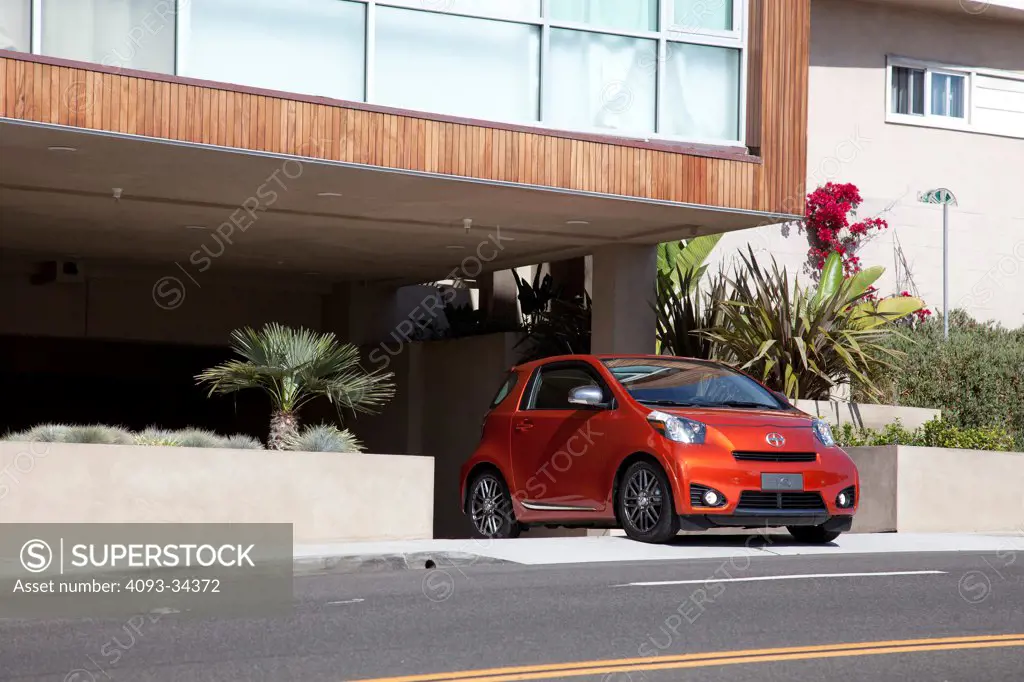 Front 3/4 static view of an orange 2012 Scion IQ parked in front of a garage of a modern home.