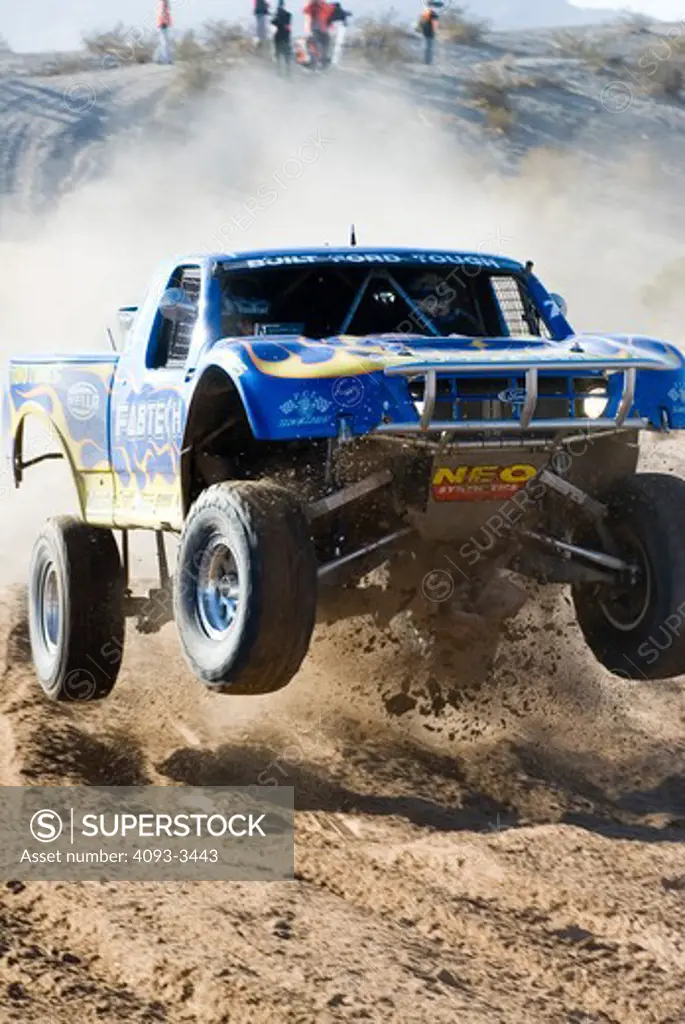 Baja desert race trucks spinning and kicking up dirt and dust.  Going off of a jump and in mid air