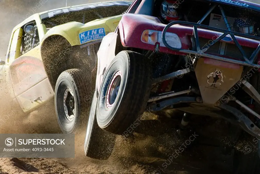 Baja desert race trucks spinning and kicking up dirt and dust.  Going off of a jump and in mid air