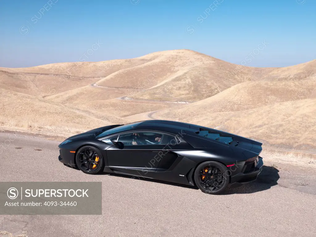 Rear 7/8 static view of a satin black 2012 Lamborghini Aventador on a rural mountain road.